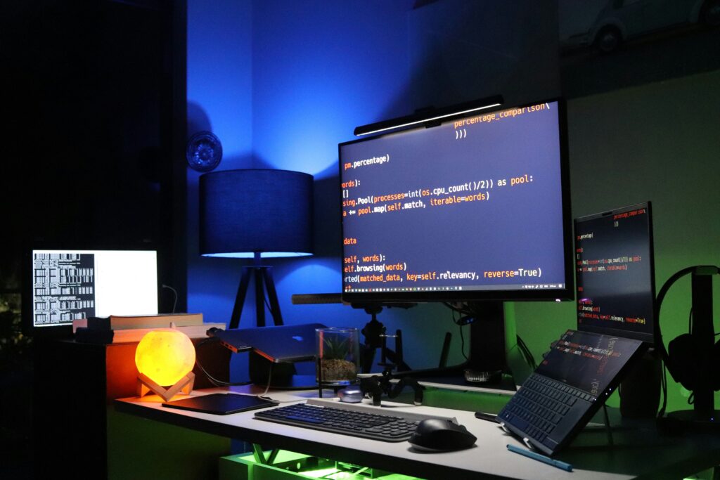 Desk with two monitors showing Python code, lit in deep blue and warm orange