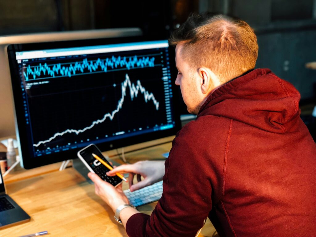 Analyst in a red hoodie studying a rising market chart on a large monitor